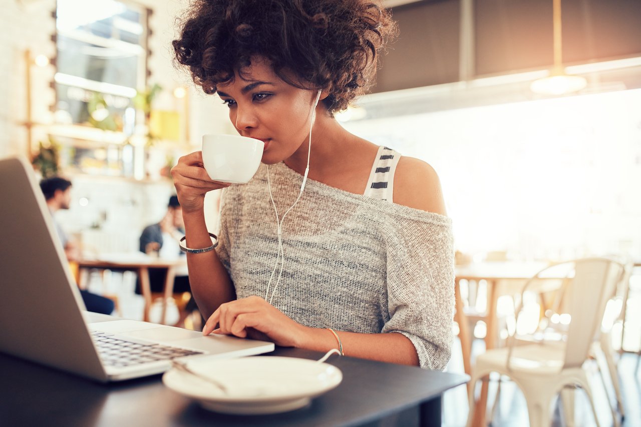 kobieta pijąca kawę z muzyką na komputerze w Residences Tulip współtworząca przestrzeń ©shutterstock